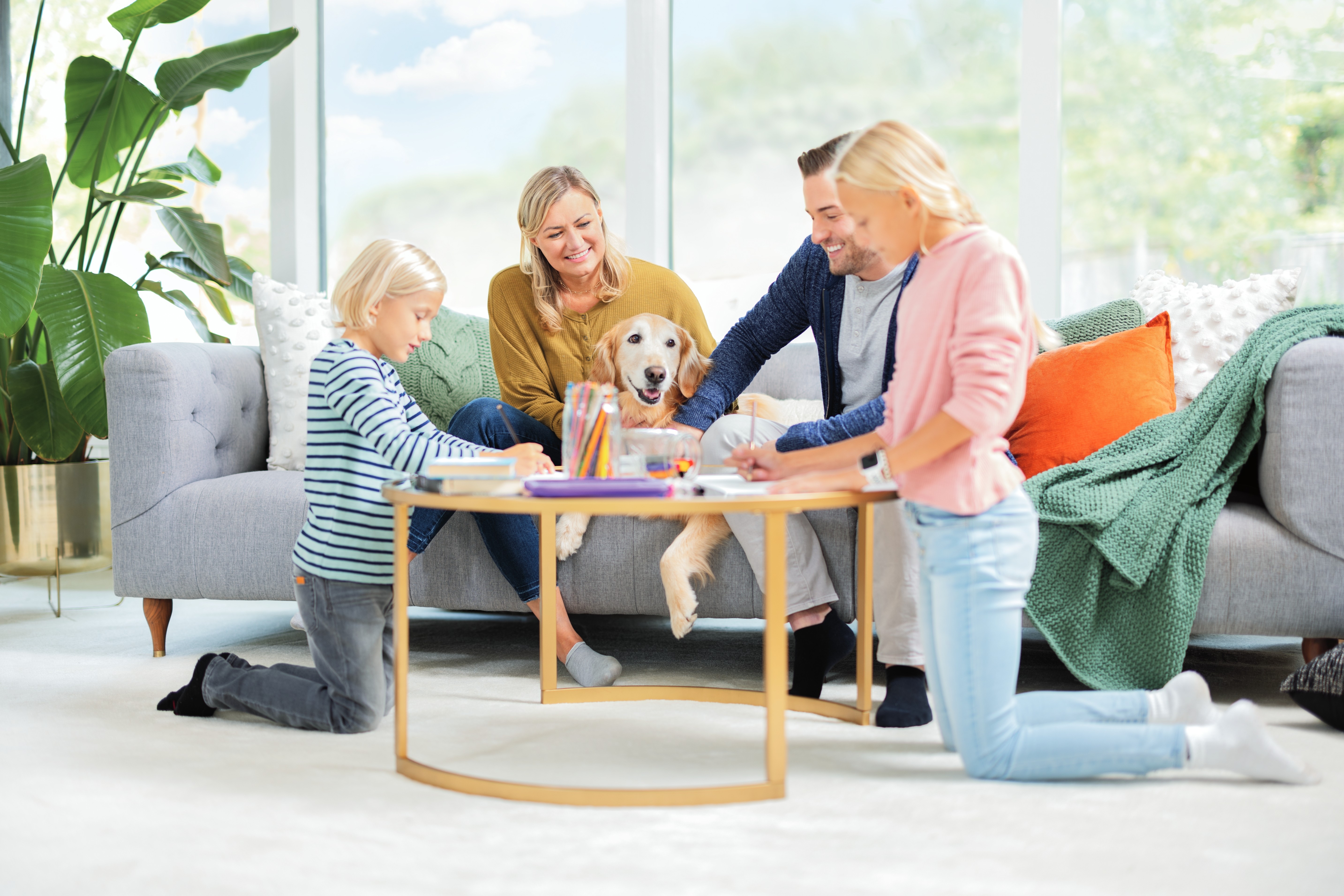 Family and dog sitting around table on carpet. 