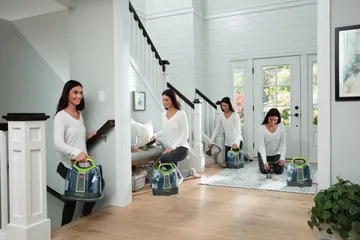 Woman using portable deep cleaner to clean stain off area rug, stairs, and couch.