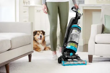 CleanView Swivel Rewind Pet Vacuum vacuuming carpet between furniture.
