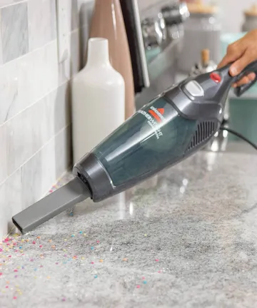 Using Featherweight Stick Vac has hand vac with crevice tool vacuuming couch cushions