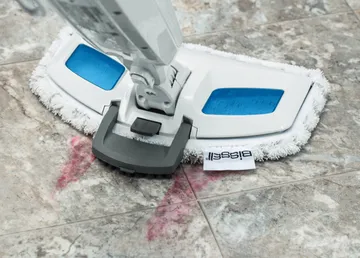 Using Scrubbing Brush on foot to steam sticky mess on tile flooring.