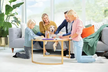 Family and dog sitting around table on carpet in living area.