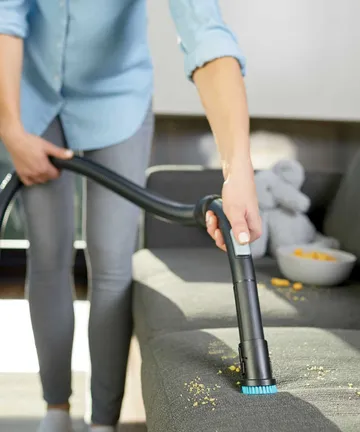 Using dusting brush on hose to vacuum crumbs off couch cushion