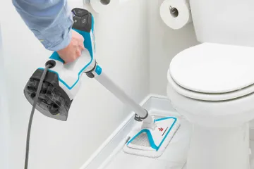 Using PowerFresh Slim 3-in-1 Steam Mop to mop tile flooring between wall and toilet in bathroom.