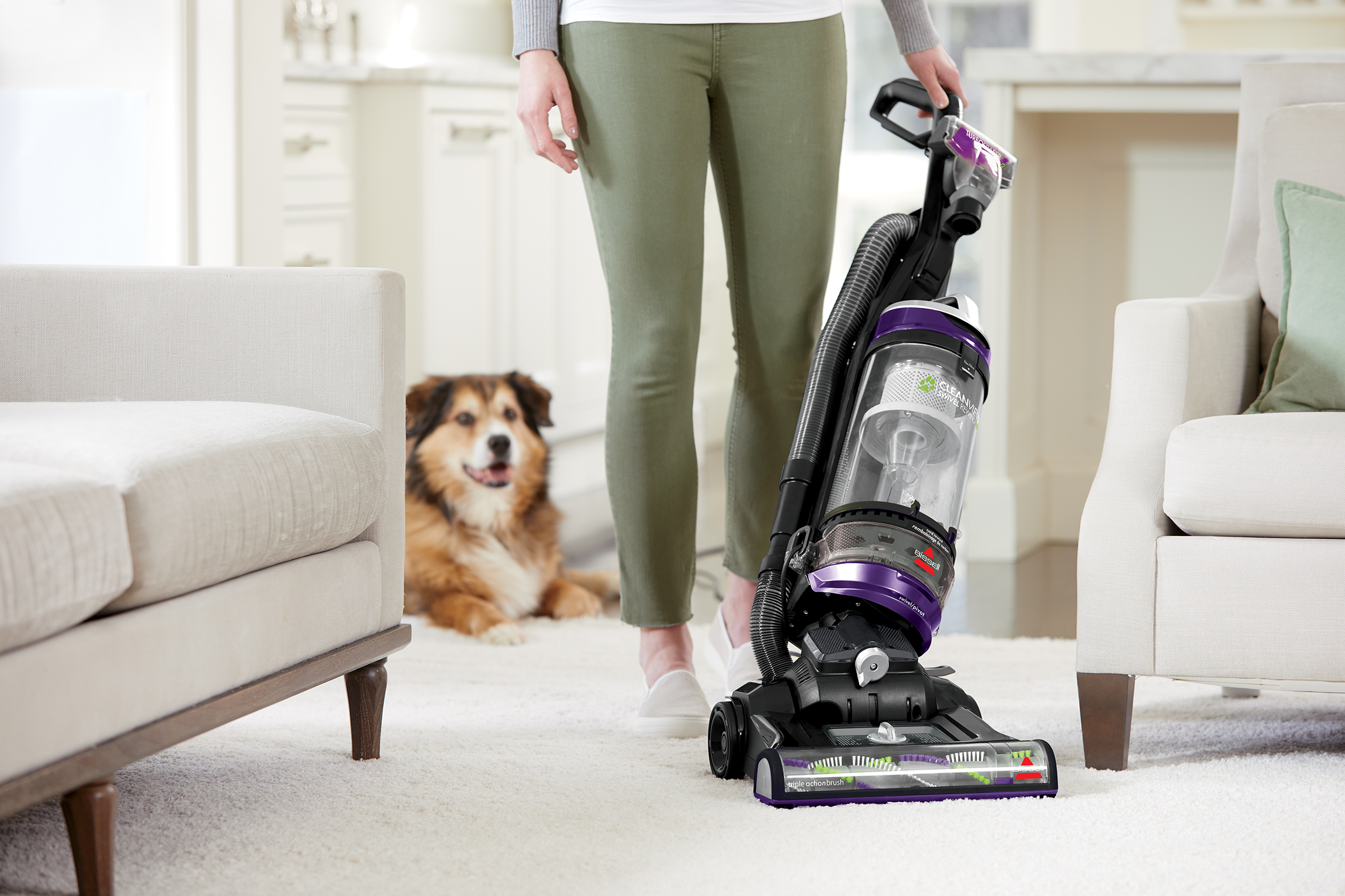 CleanView Swivel Rewind Pet Vacuum vacuuming carpet between furniture.