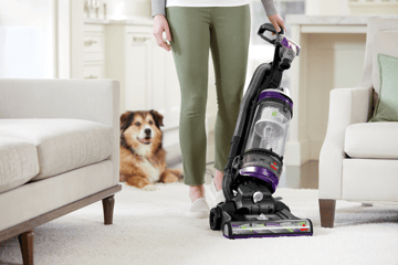 CleanView Swivel Rewind Pet Vacuum vacuuming carpet between furniture.
