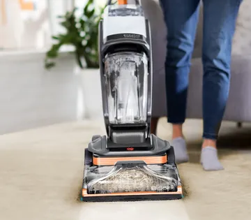 Woman using BISSELL Revolution HydroSteam carpet cleaner to remove deep stains from white carpet